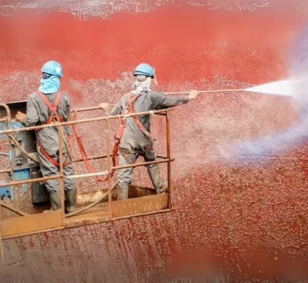 Workers using high-pressure water jet to clean a ship hull surface for maintenance and coating preparation.