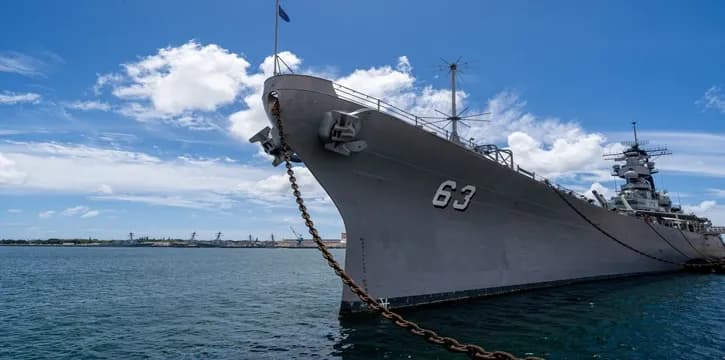 Large naval battleship number 63 anchored in harbor under clear blue sky and calm sea.
