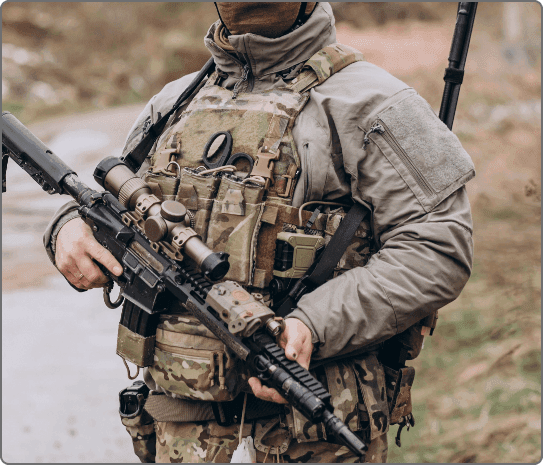 Soldier in tactical camouflage uniform holding rifle and wearing modular body armor vest with combat gear.